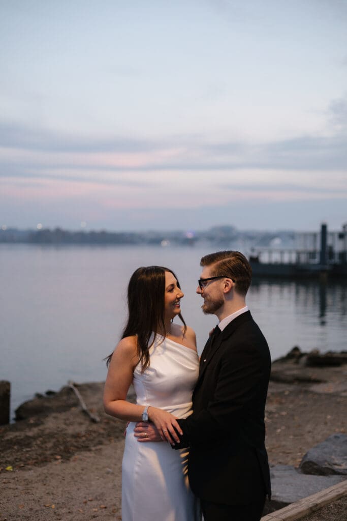Newlywed couple silhouetted against the warm 
sunset sky on the Potomac waterfront in Old Town 
Alexandria during their casual fall elopement — 
Northern Virginia elopement photographer 
Kelly Wineinger Creative