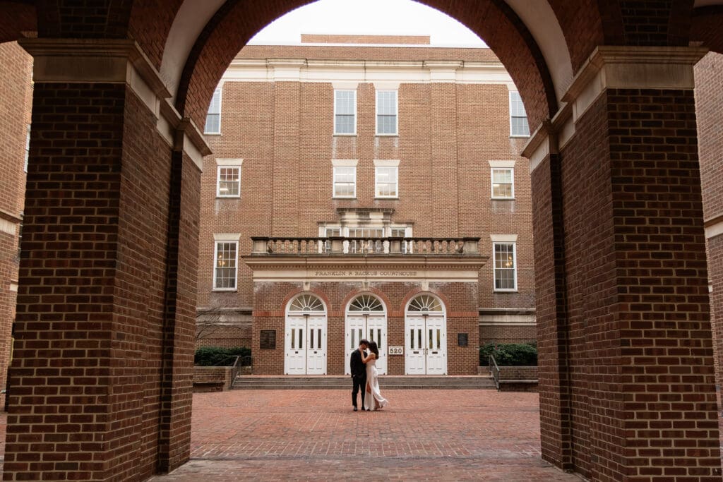 Couple embracing in front of the classic brick arches of the Alexandria Virginia Courthouse 
during their Old Town elopement at golden hour — Northern Virginia elopement photographer 
Kelly Wineinger Creative