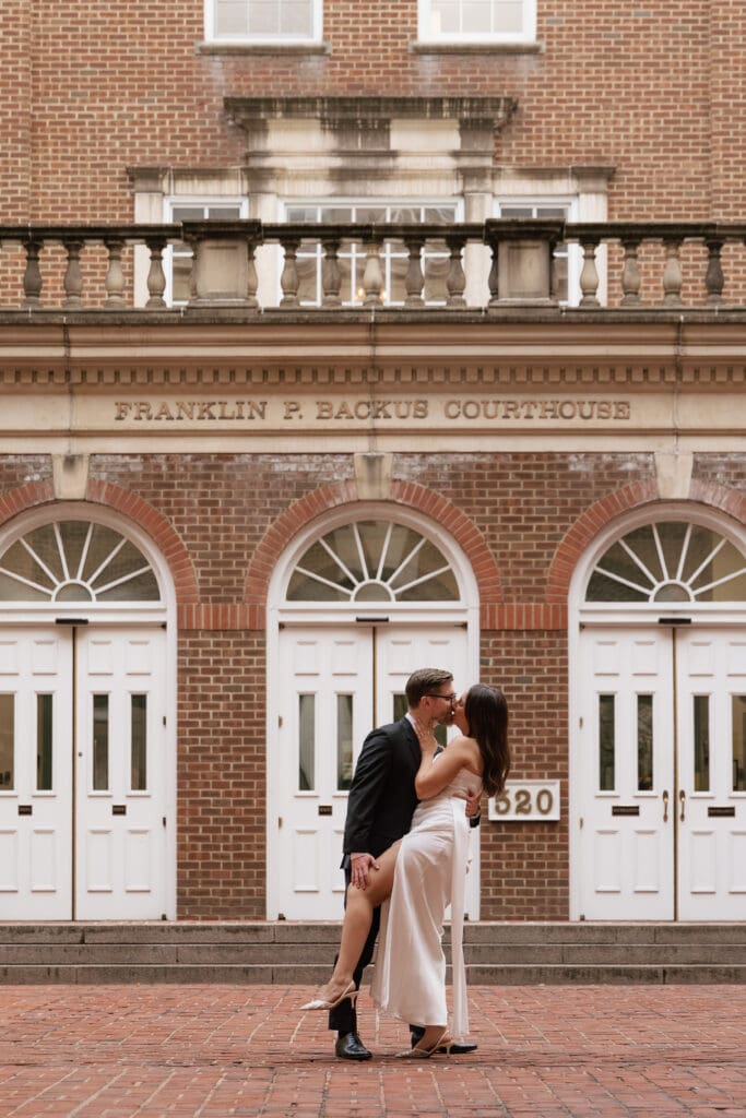 Bride and groom sharing a romantic kiss under the sweeping arched portico of the Alexandria 
Courthouse in Old Town Virginia during their intimate elopement — Kelly Wineinger Creative