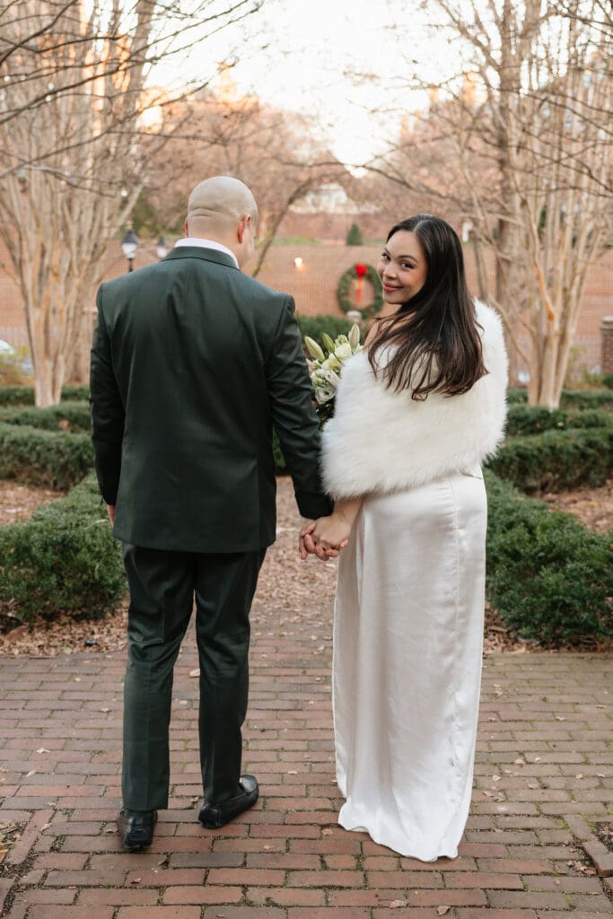 bride glances over her shoulder while walking with her husband during wedding portraits