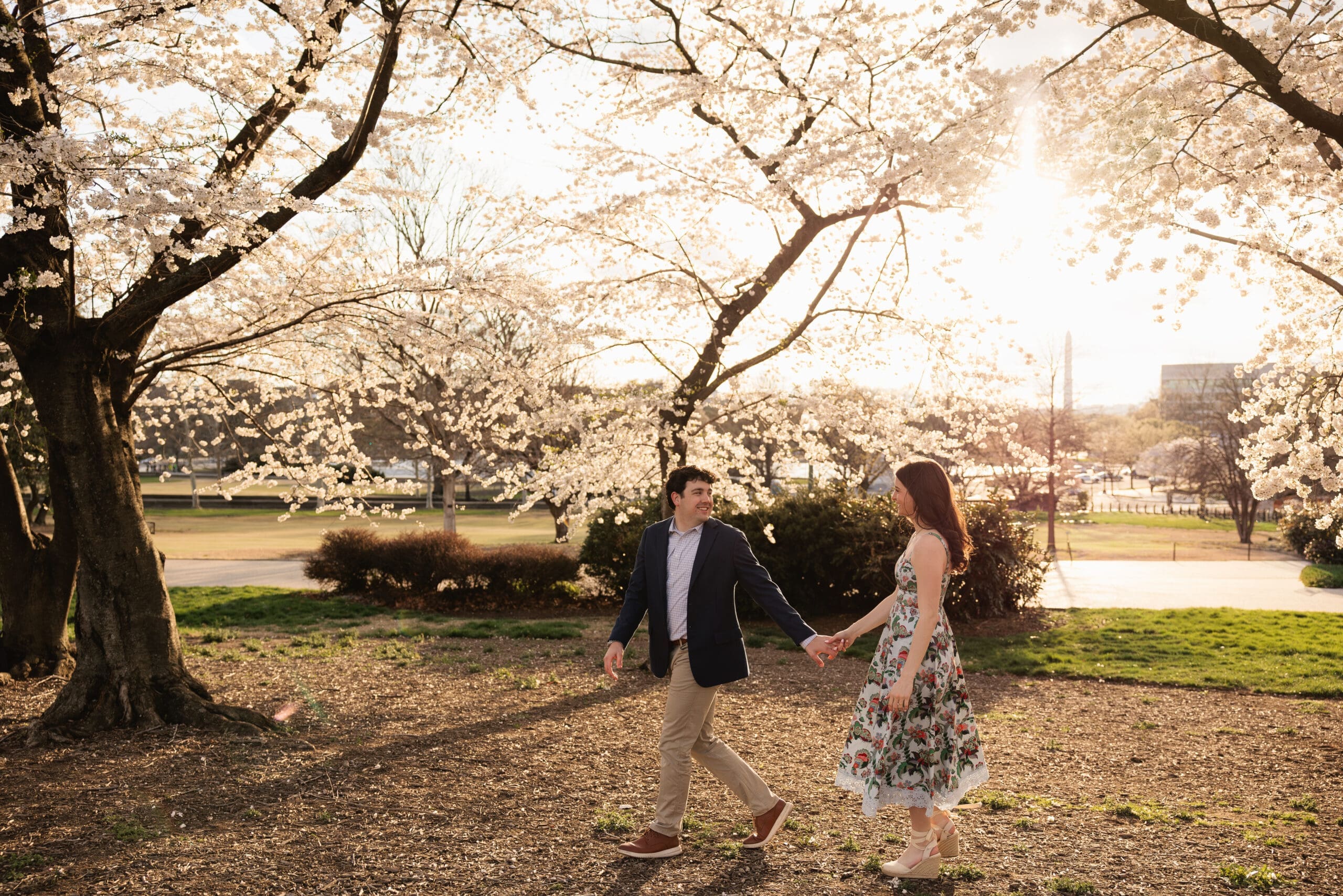 couple walks hand in hand for an engagement photoshoot during golden hour with views of the DC monuments in the background.