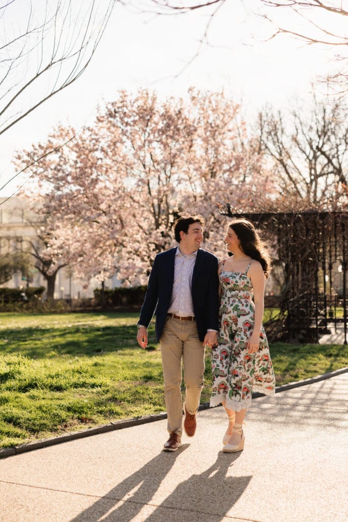 Couple walks hand in hand in front of the U.S. Capitol building during a spring engagement photoshoot.
