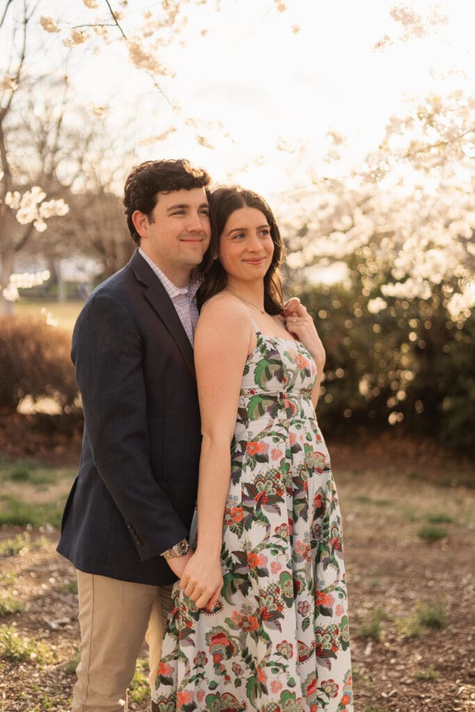 couple poses for an engagement photo in front of the iconic DC cherry blossoms during golden hour
