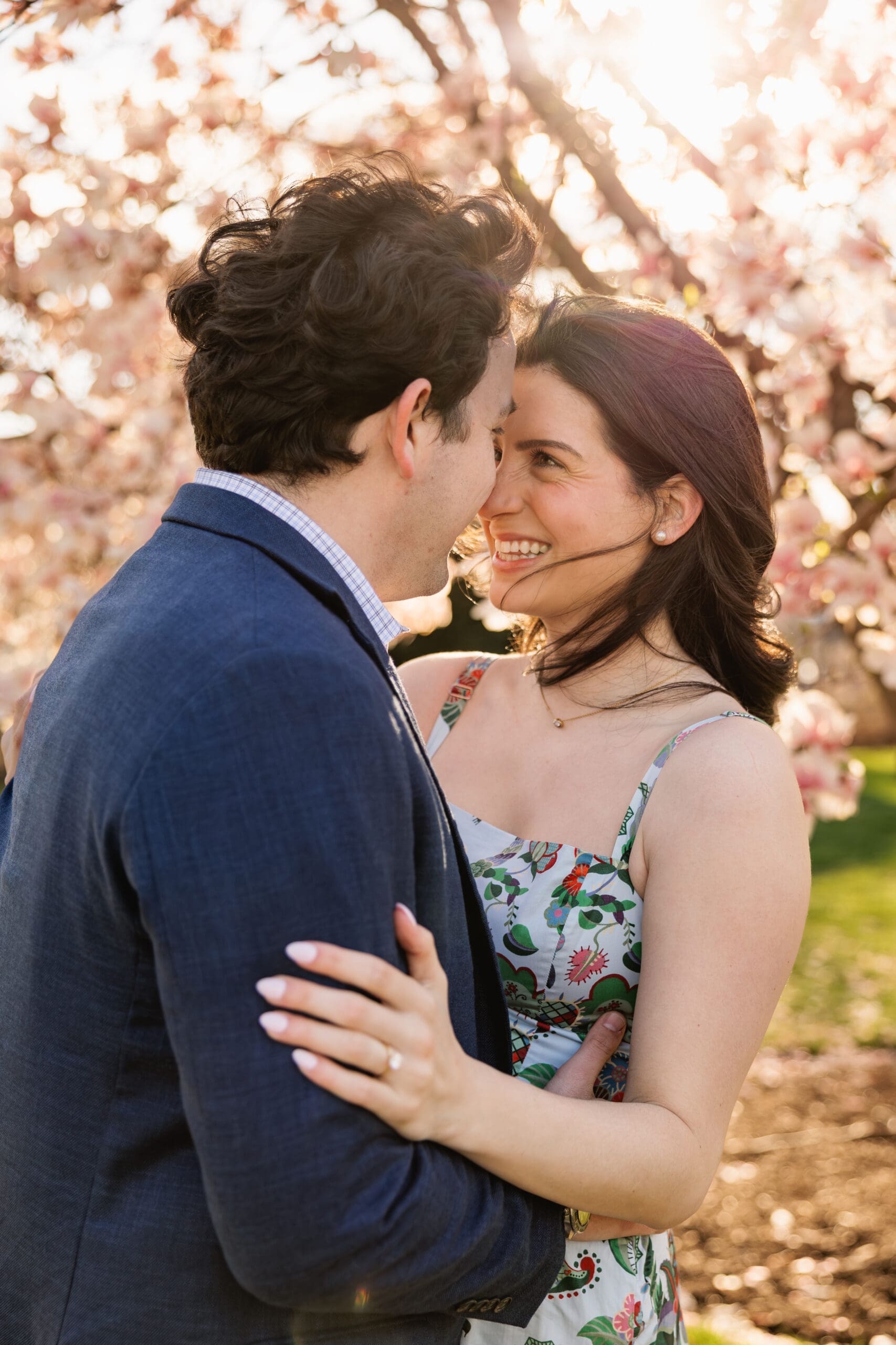 Couple smiles at each other in from of blooming saucer magnolia tree in front of the DC Capitol building during engagement photos