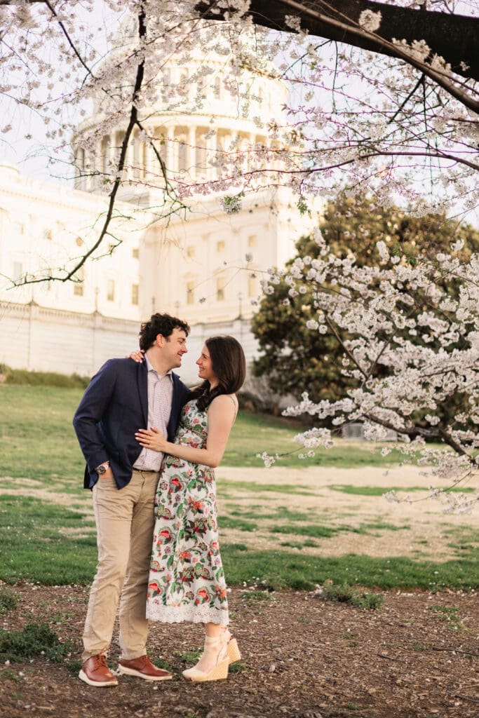 Couple smiles at each other for a sweet engagement photo in front of the US Capitol building in Washington DC