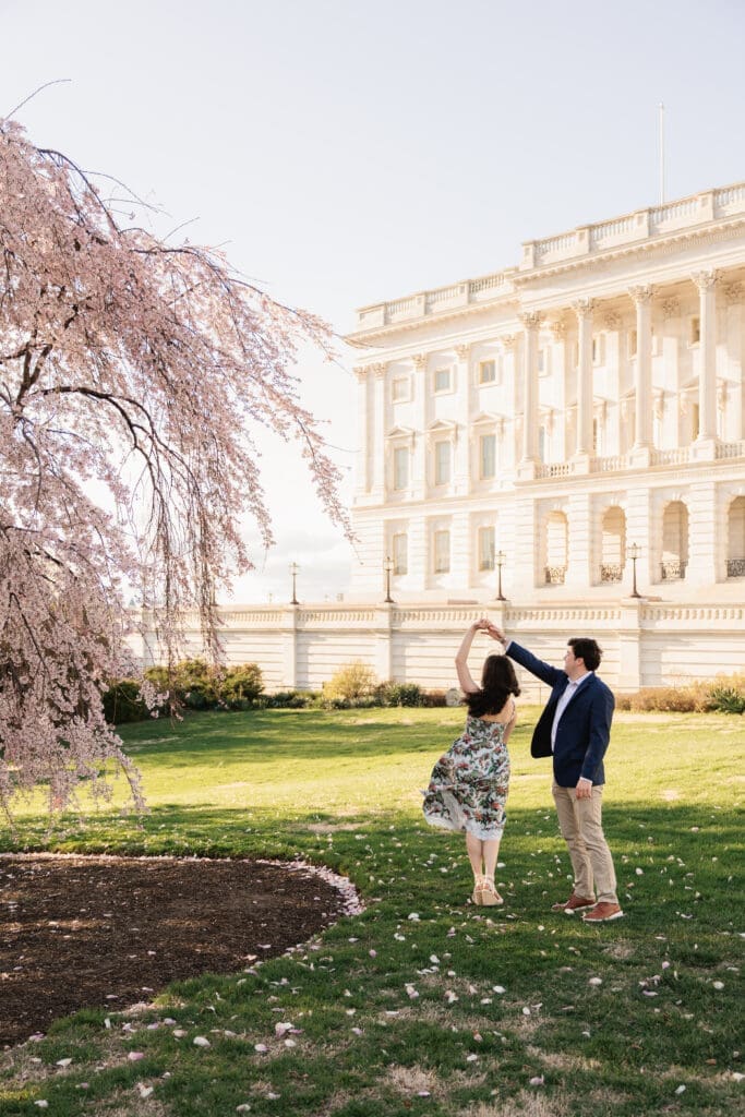 Man twirls his fiancee in front of the US Capitol building during a spring engagement photoshoot